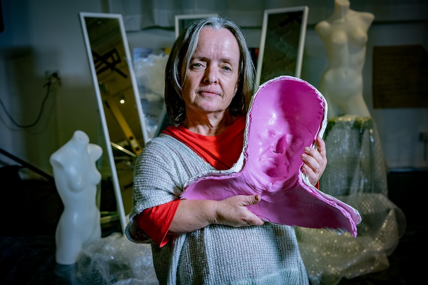 Leisa holds a pink mould of her face, in a portrait taken in the studio.