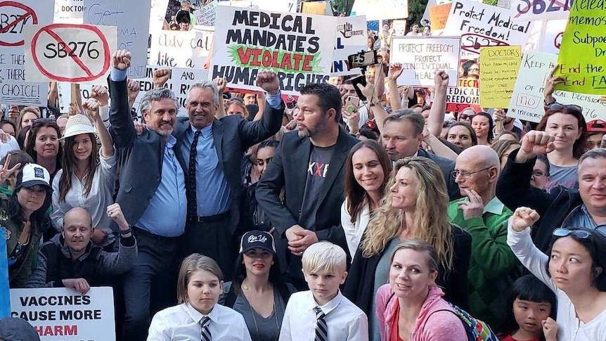 People with raised hands and hold signs at an anti-vaccine rally in America.