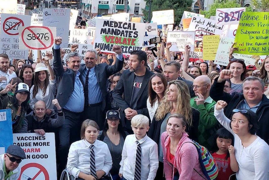 People with raised hands and hold signs at an anti-vaccine rally in America.