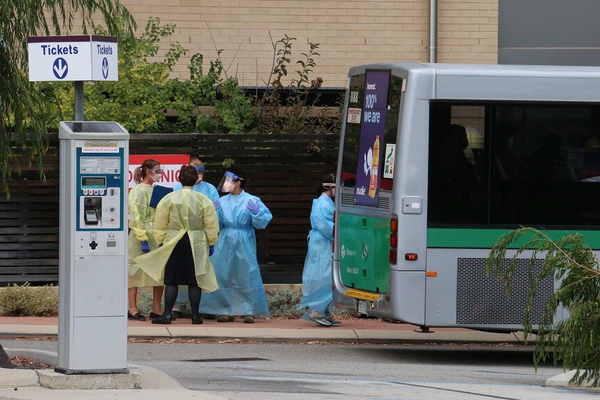Medical workers in plastic gowns an PPE gear stand at the rear of a Transperth bus outside Joondalup Private Hospital.