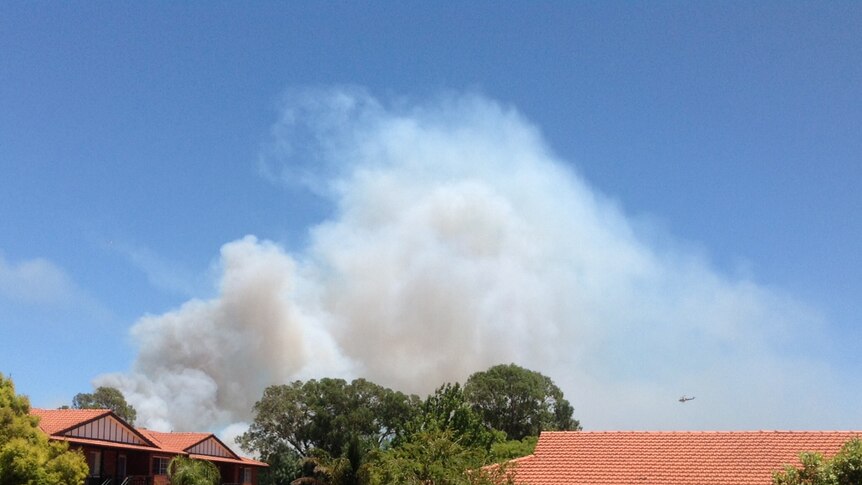 Smoke from a fire burning in Perth's western suburbs billows above the roofs of houses nearby.