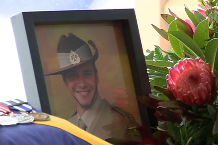 A picture of a smiling young soldier next to his coffin.
