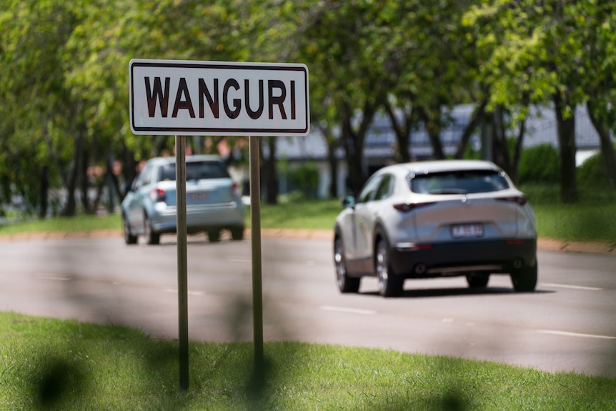 a street sign saying wanguri with cars driving past