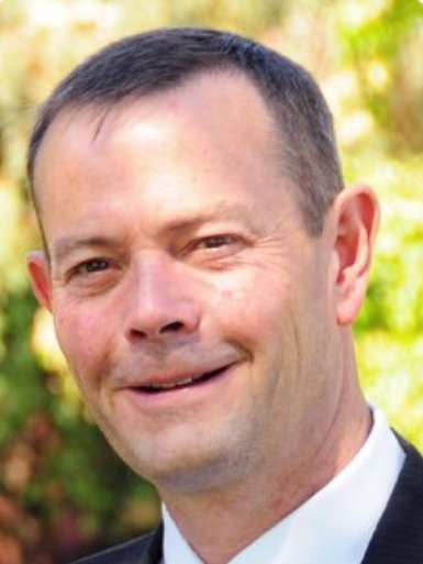 Portrait of middle-aged man with short, brown hair wearing a suit and smiling.