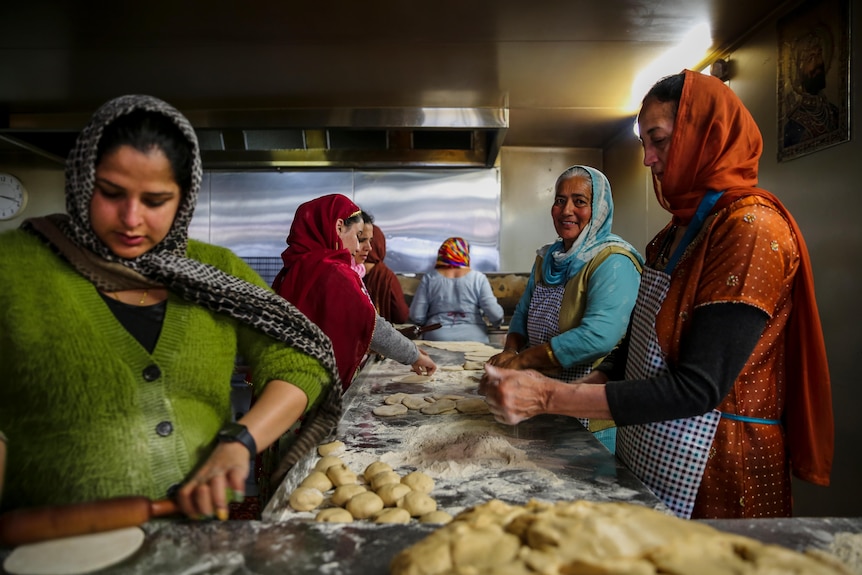 Women in colourful clothing stand around a table preparing food for Diwali celebrations.