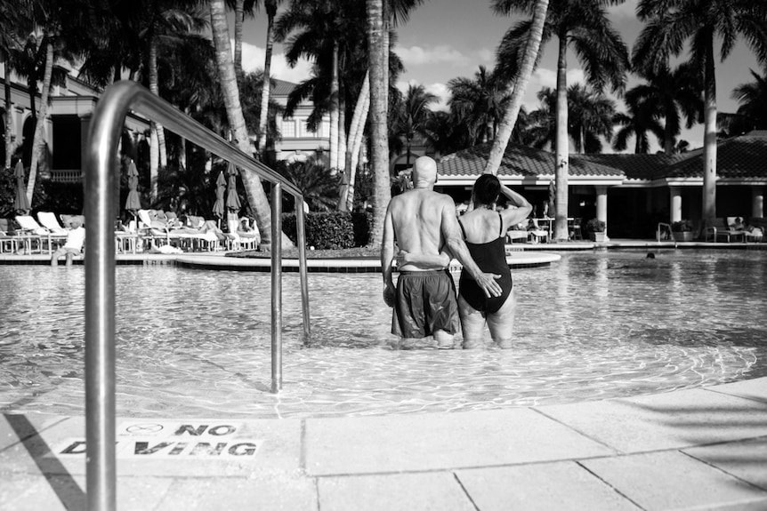 Laurel and Howie Borowick in swimmers, standing knee deep in a pool at a tropical-style resort.