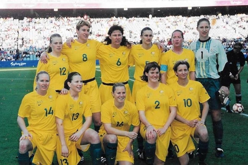 A women's soccer team wearing yellow and green poses for a photo before a game in a stadium