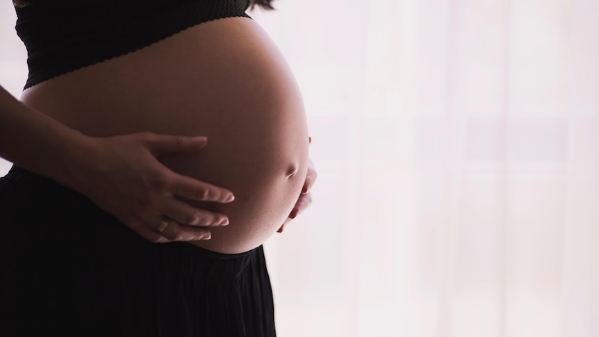 Someone holds their pregnant belly that's poking out of their workout outfit