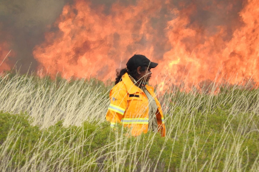 Female Aboriginal ranger stands in front of flames