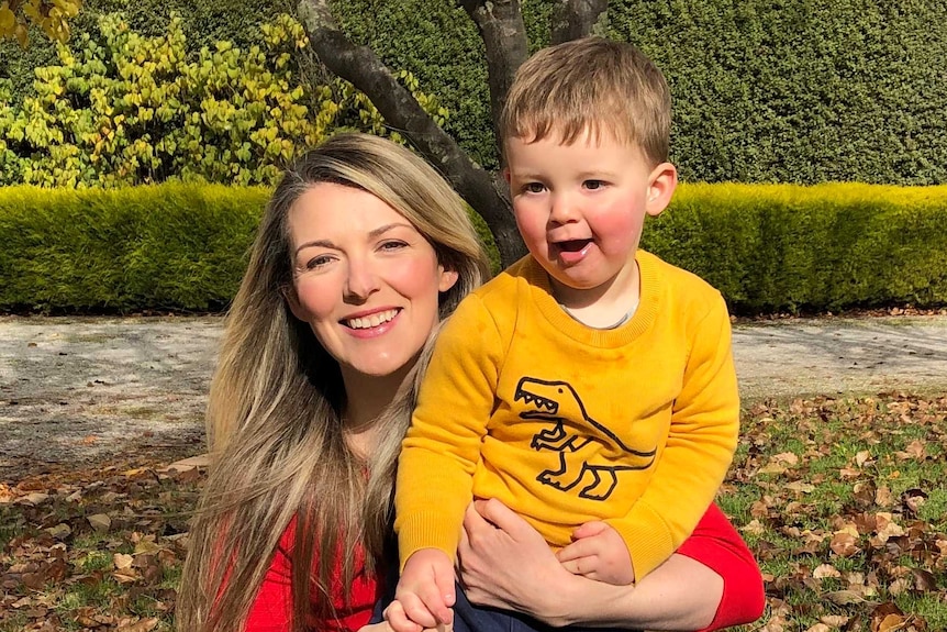 Woman in red shirt holding toddler in yellow shirt