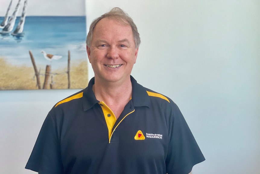 John Bates stands in front of a beach painting smiling.