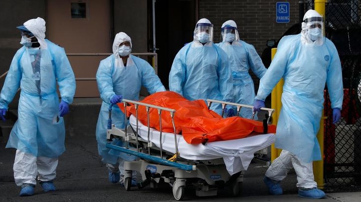 Health care workers wheel out a body of a dead person covered in an orange sheet.