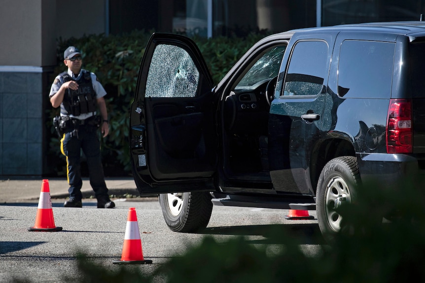 A police officer stands near a vehicle with bullet holes