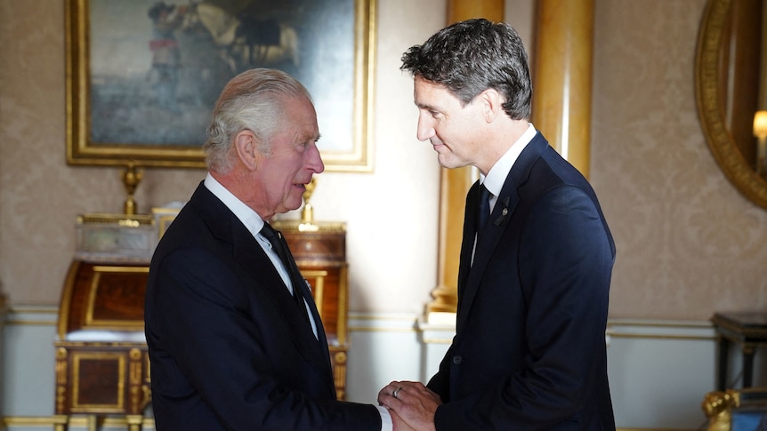 An elderly man in a suit with slicked-back grey hair and a younger man with dark hair shake hands in a posh-looking room.