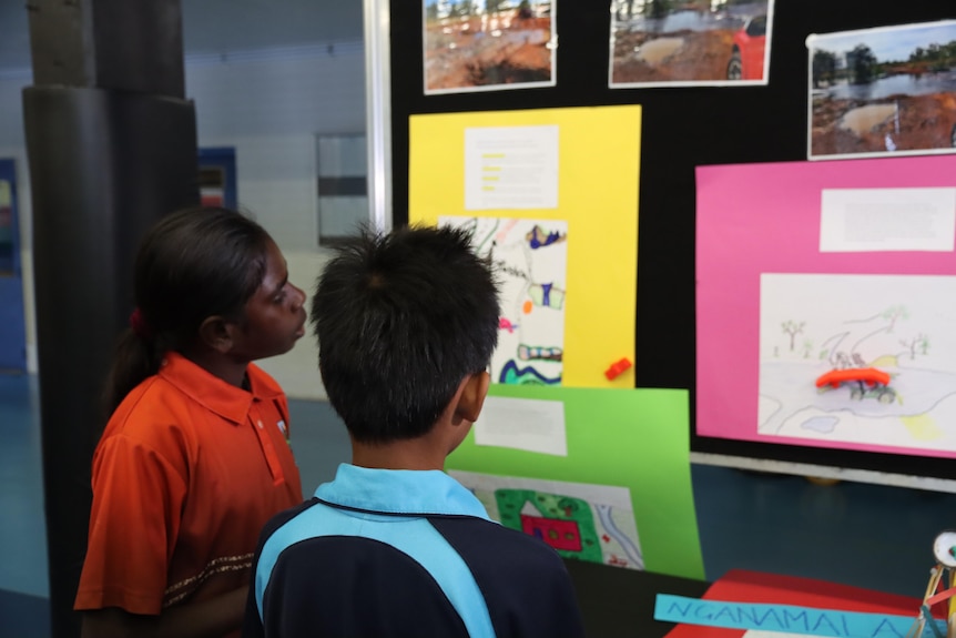 A girl and a boy in school uniforms look at a science display on a board