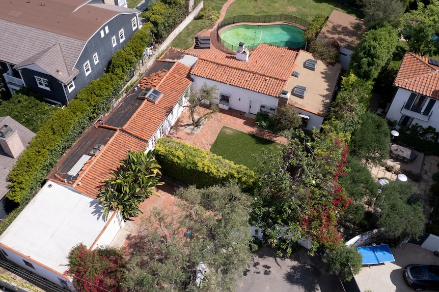 An aerial view of a one-story house with terracotta tile roof and a kidney bean shaped pool out the back 