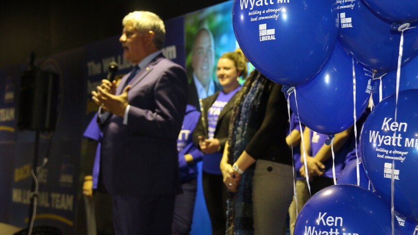 A clutch of blue balloons with Ken Wyatt's name on them on a stage in front of the Liberal MP as he speaks to an unseen crowd.