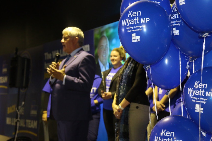 A clutch of blue balloons with Ken Wyatt's name on them on a stage in front of the Liberal MP as he speaks to an unseen crowd.