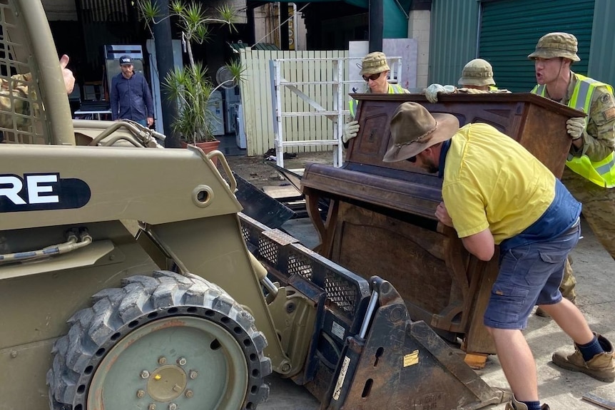men lifting a piano onto a bulldozer
