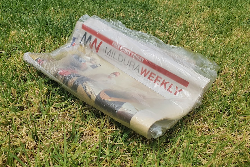 A newspaper in plastic on a lawn.