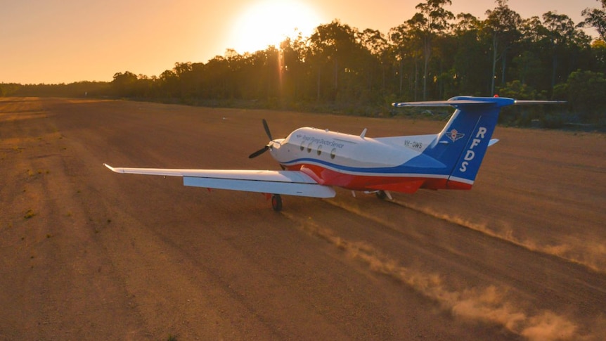 An RFDS plane takes off from a red dirt runway.
