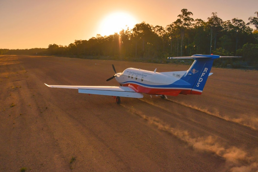 An RFDS plane takes off from a red dirt runway.