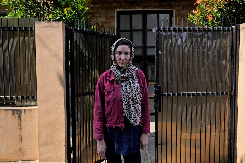 Afghan women stands in front of gate to a house.