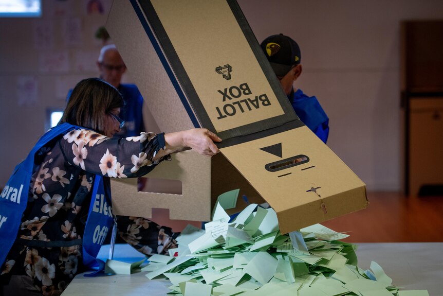A man and woman in blue electoral commission shirts empty a ballot box full of votes