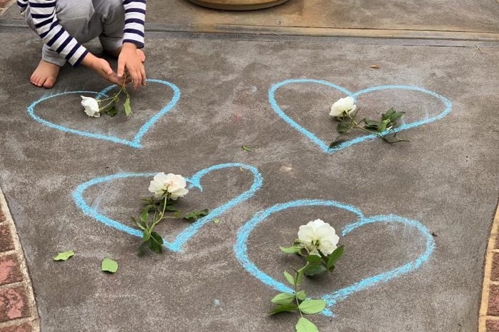 A child draws blue hearts around white flowers in the driveway of a home.