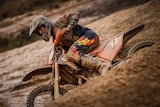 man riding dirt bike covered in mud, going around a bend
