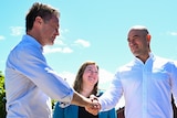 Two men and a woman, shaking hands in front of a school 