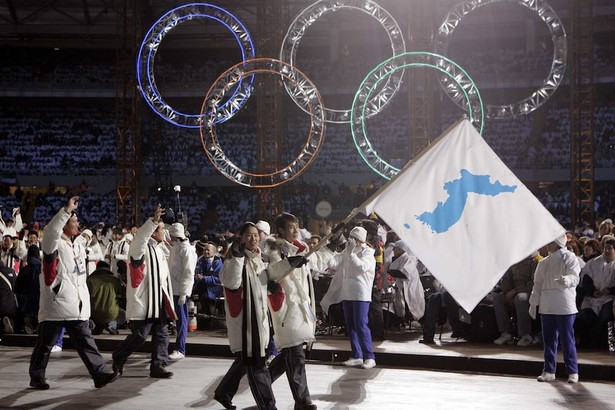 Korean flag-bearer's Bora Lee and Jong-In Lee walk side by side holding blue and white flag under Olympic rings