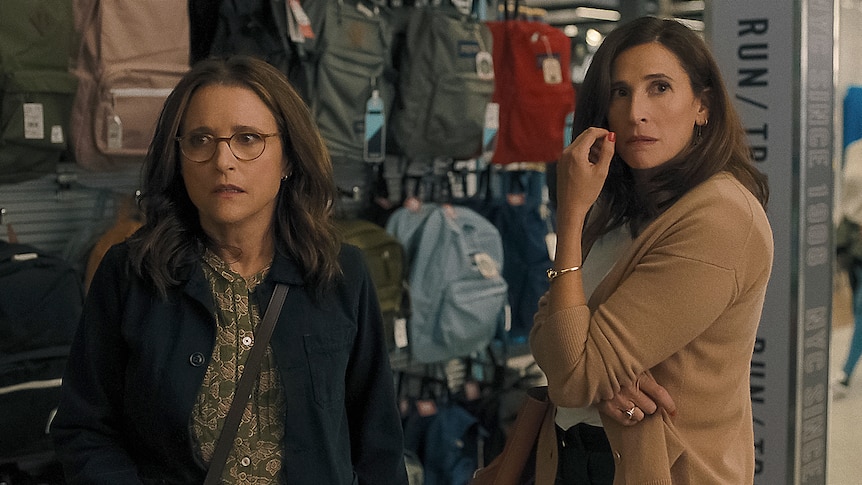 A middle-aged brunette white woman with glasses stands next to another middle-aged brunette woman in a store, looking perturbed.