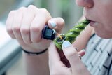 A woman taking a hit from a small glass marijuana pipe.