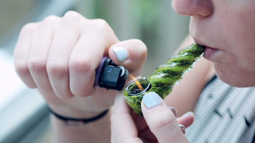 A woman taking a hit from a small glass marijuana pipe.