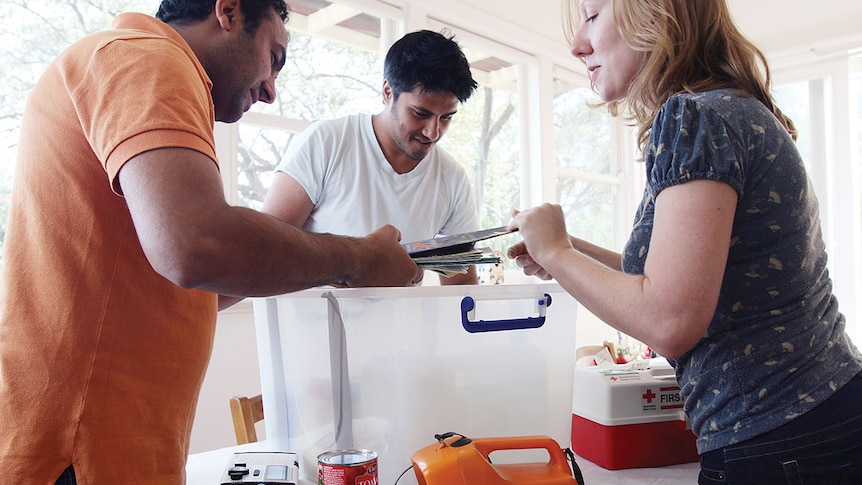 Three people loading items like torches, canned food and first aid kit into a plastic tub.