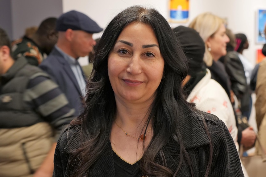 Hind Suleiman stands in the foreground of a moving crowd smiling at the camera. 