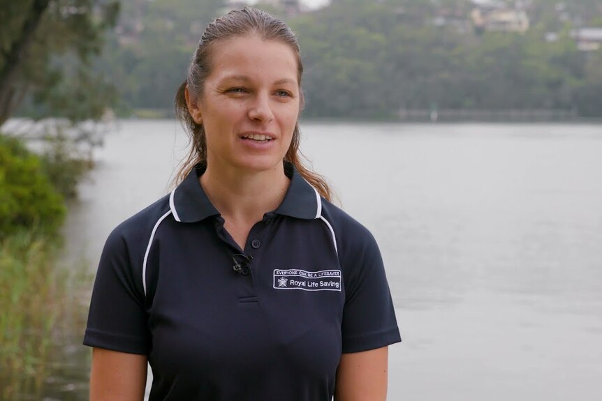 a woman with brown hair wearing a navy shirt in front of a lake.