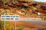 Red dirt at the side of the road with a sign that says 'Hope Downs mine 30km'