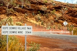 Red dirt at the side of the road with a sign that says 'Hope Downs mine 30km'