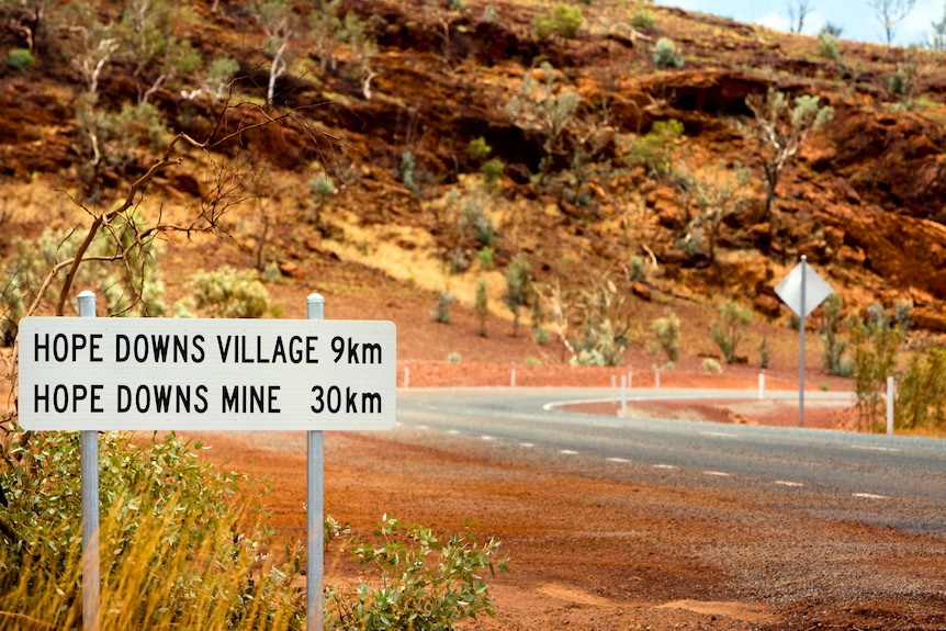 Red dirt at the side of the road with a sign that says 'Hope Downs mine 30km'