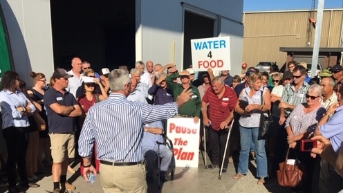 Protestors hold signs calling for a pause in the Murray Darling Basin Plan as a man addresses them