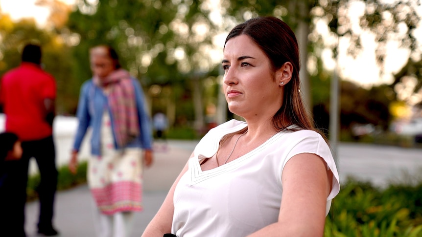 A young woman sits on a park bench looking off to the distance. 