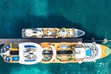 Aerial shot of a very large and much smaller cruise ship over green, blue ocean.