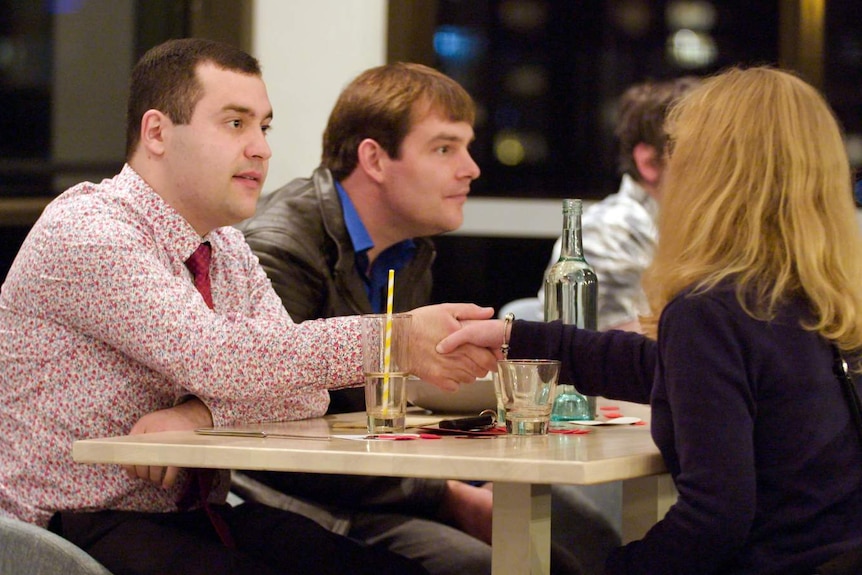 A young man shakes hands with a woman across a table as they meet at a dinner date