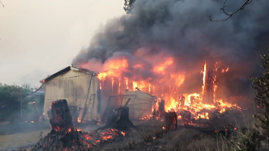 A bush property on fire, with home that has flames homing from the roof.