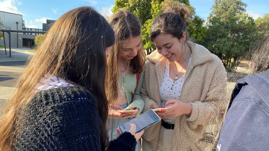 A picture of three female students checking their VCE results on their phones.
