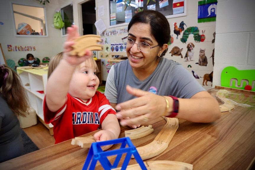 A female childcare worker sitting next a young toddler who is playing with toys