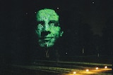 A large face is projected onto the canopy of a tree