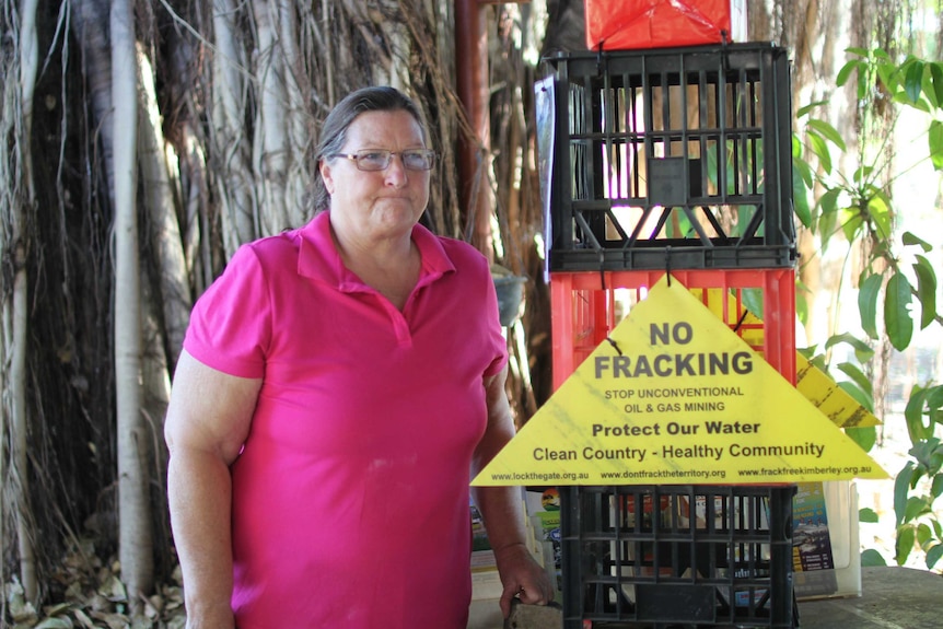 a woman standing beside a "no frakcing" sign with a tree behind.